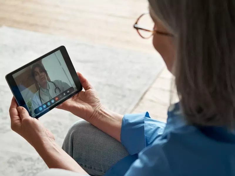 Woman sitting in her living room, holding a tablet as she consults with a virtual care provider about her symptoms