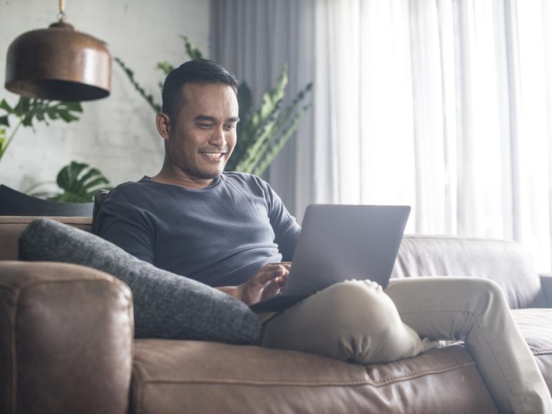 Man sitting on a couch, smiling down at his laptop while completing an eVisit questionnaire