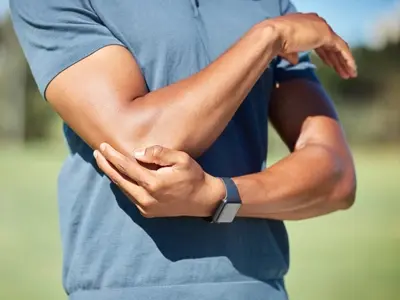 A man standing outside with elbow pain after bending and straightening it