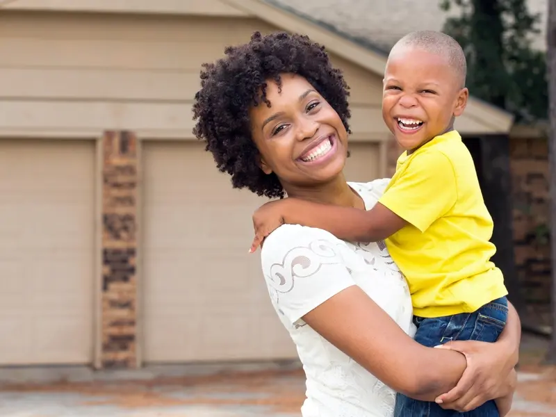 A mother holds her son, as they both grin towards the camera