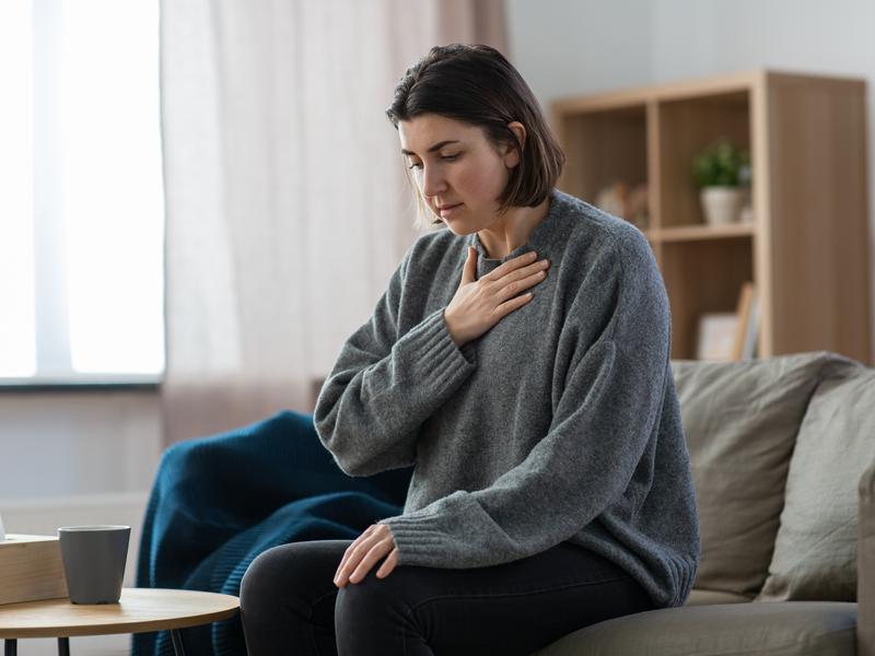 Woman with depression sitting on a couch, holding her hand to her chest as she tries to calm herself