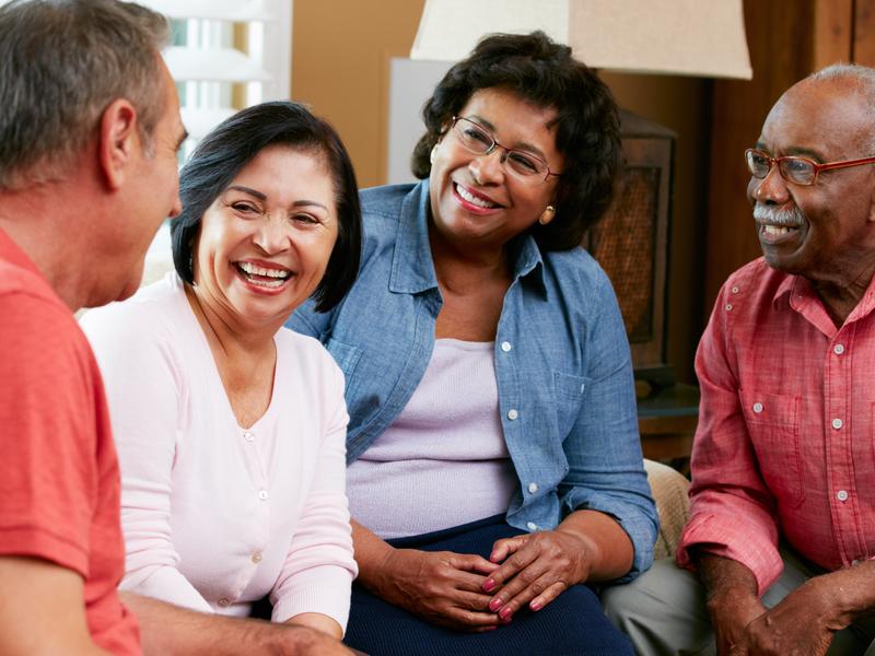 Group of older friends sitting in a living room, smiling and laughing together