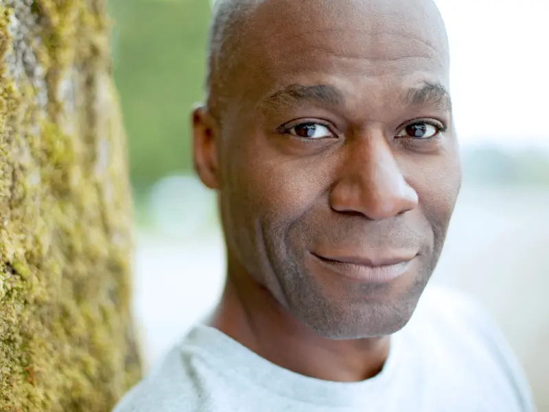 man with non-small cell lung cancer leaning on a tree smiling and looking at camera