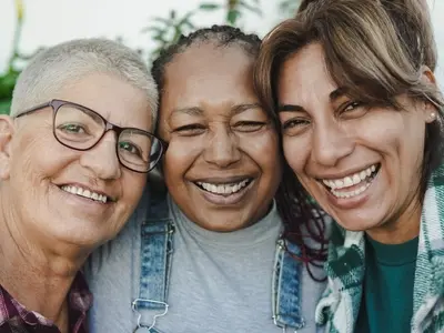 Three women with age spots standing smiling together outside