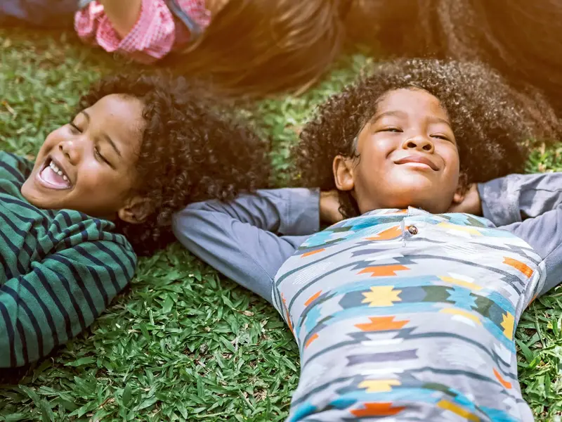 young children laying outside on the grass smiling towards the sky
