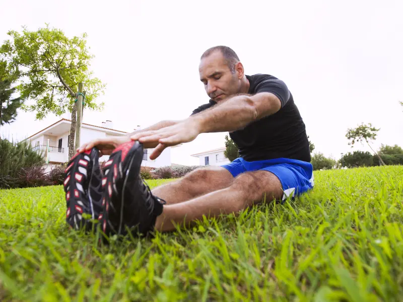 man with previous torn meniscus sitting on grass and stretching legs before running