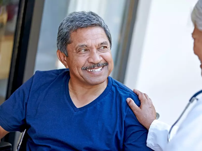 man with vascular condition sitting wheelchair smiling toward a healthcare provider