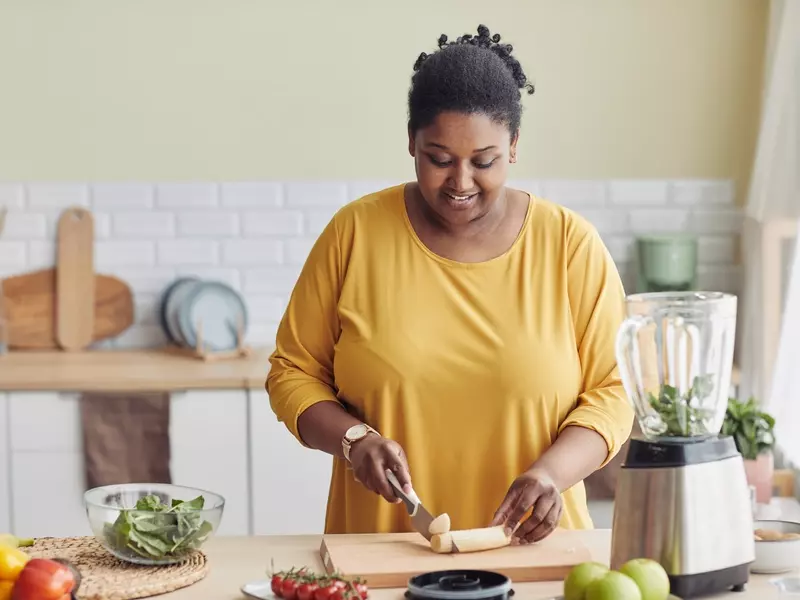 Woman slicing a banana to make a smoothie in a well-lit kitchen