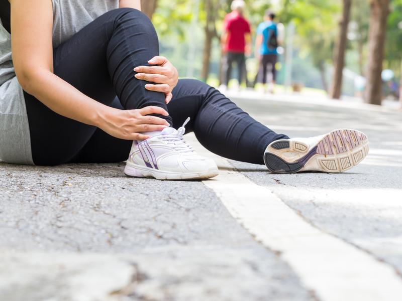 runner sitting on road on sunny day rubbing leg because of joint pain