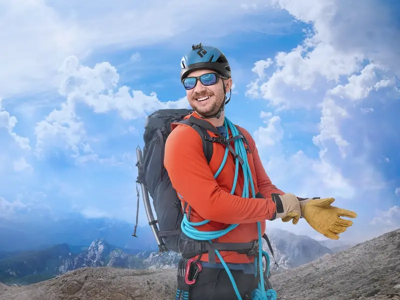 Andrew Garcia smiles above the clouds in hiking gear with a beautiful mountain view in the backgrou
