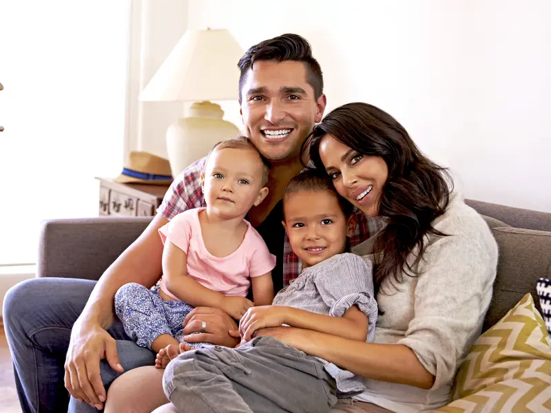 a family of four with young children sitting on couch smiling at camera