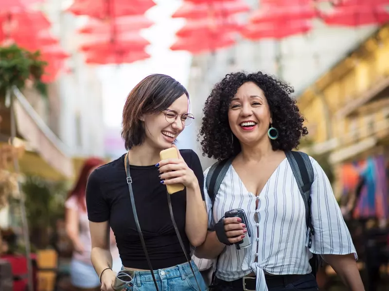 Two women with positive body image and mental health smiling and laughing as they walk through an outdoor market