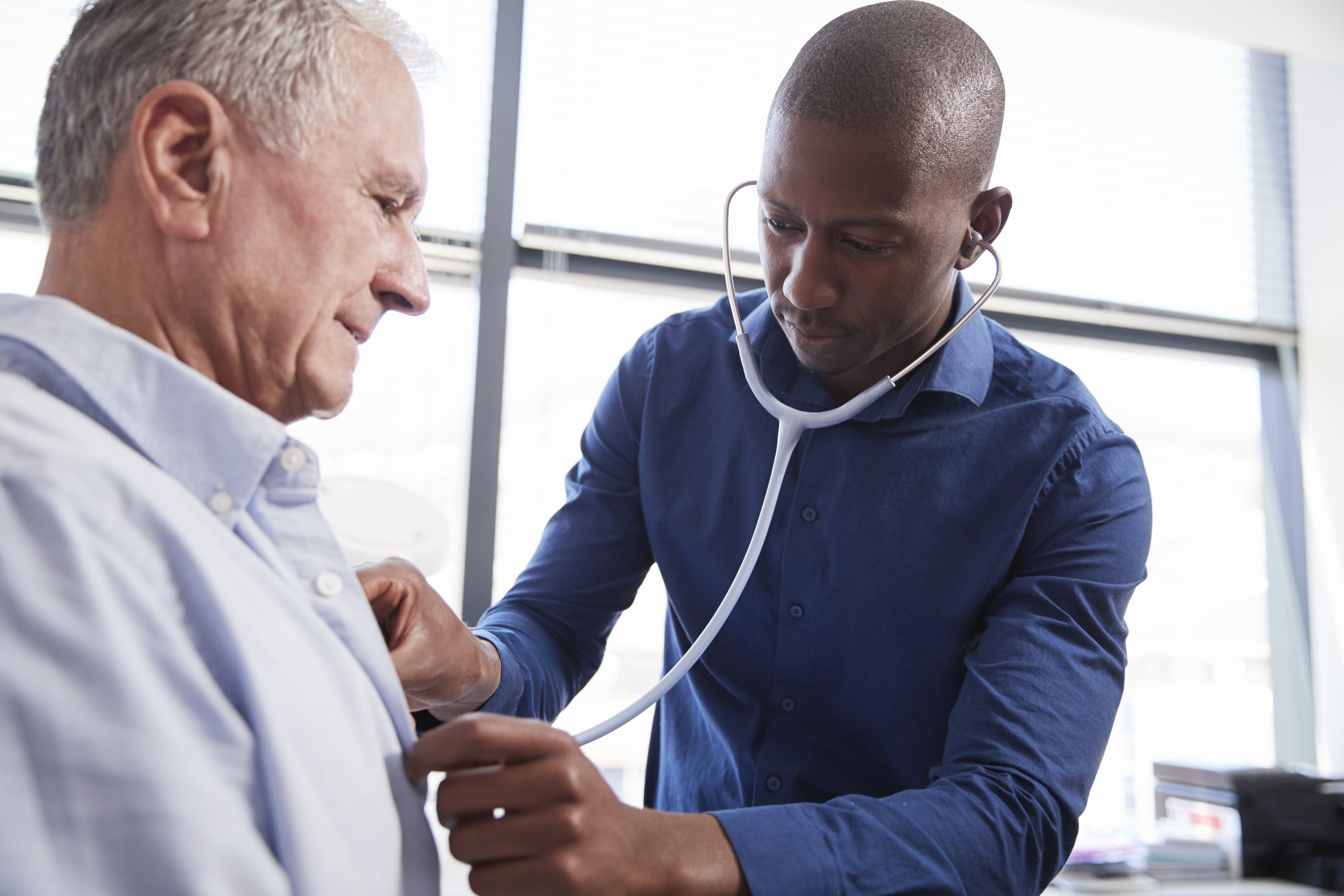 A doctor uses a stethoscope to listen to an older adult man's heart