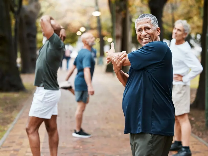 Older male recovering from CABG stretching with friends before jogging on a sunny day outdoors