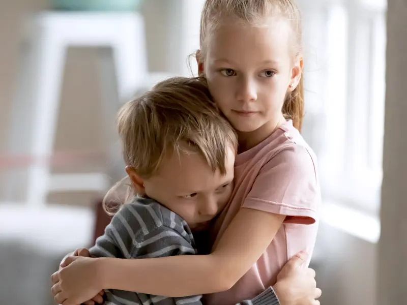 young boy and girl siblings holding onto each other with sad faces