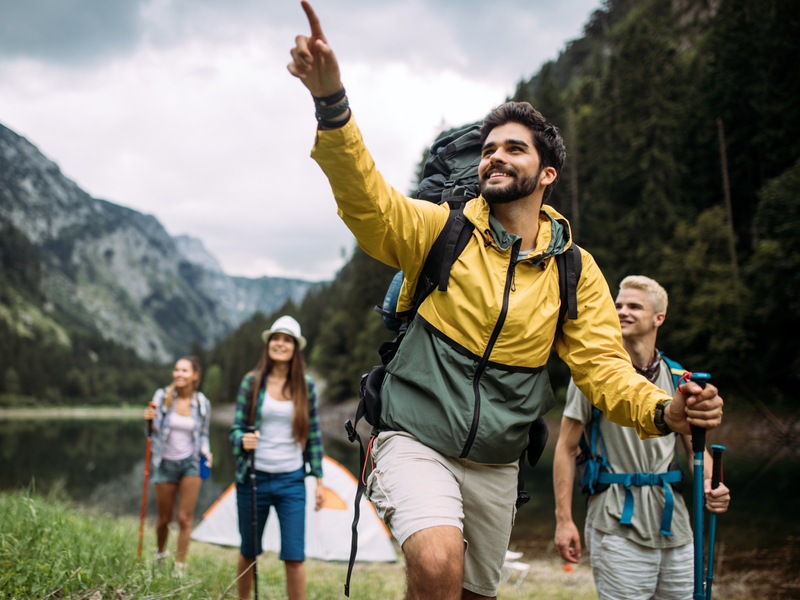 A young man points towards the mountains while hiking with three other friends