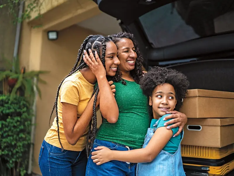 A mom and her two daughters hugging at the back of a car